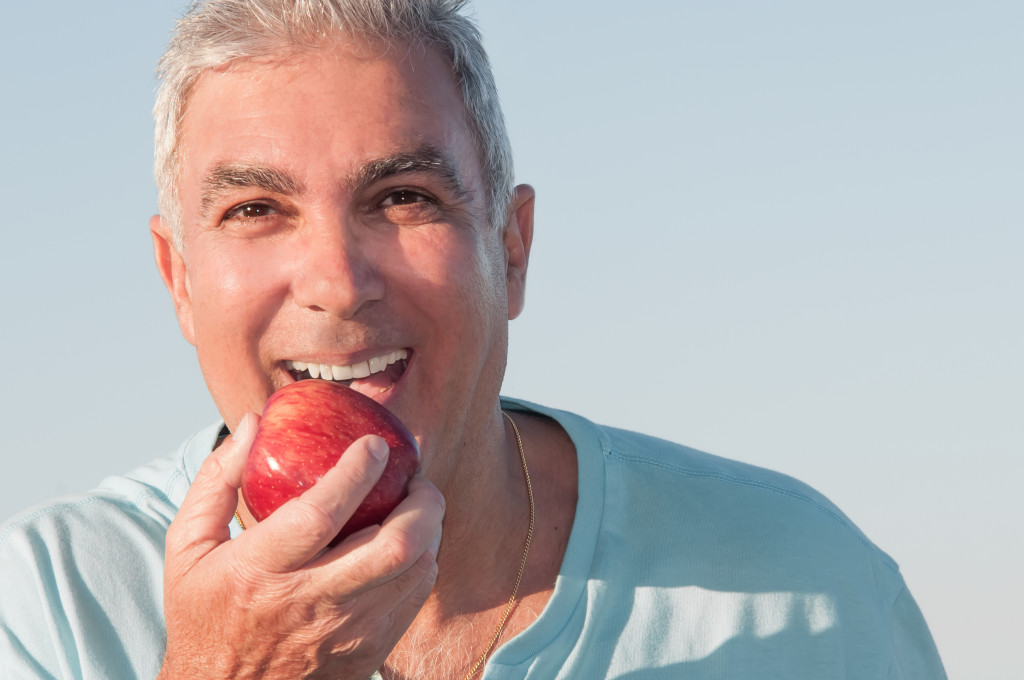 A smiling older man about to bite into a red apple