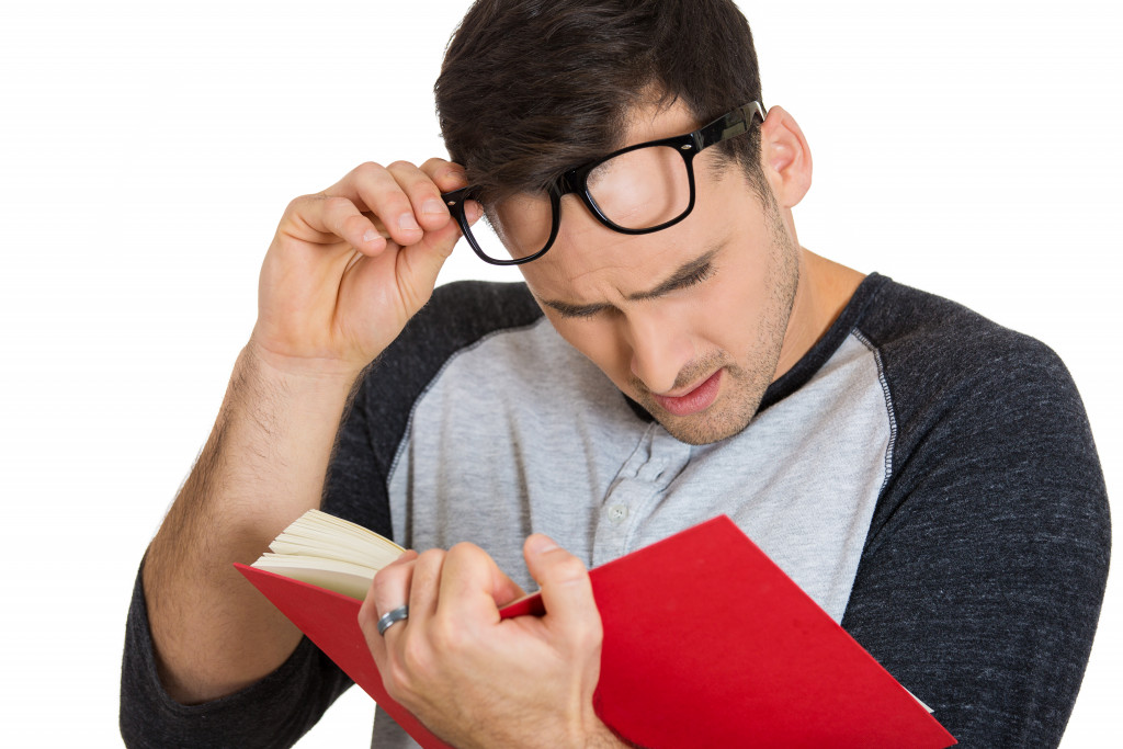 nerdy guy with glasses reading a book concept of eye problems