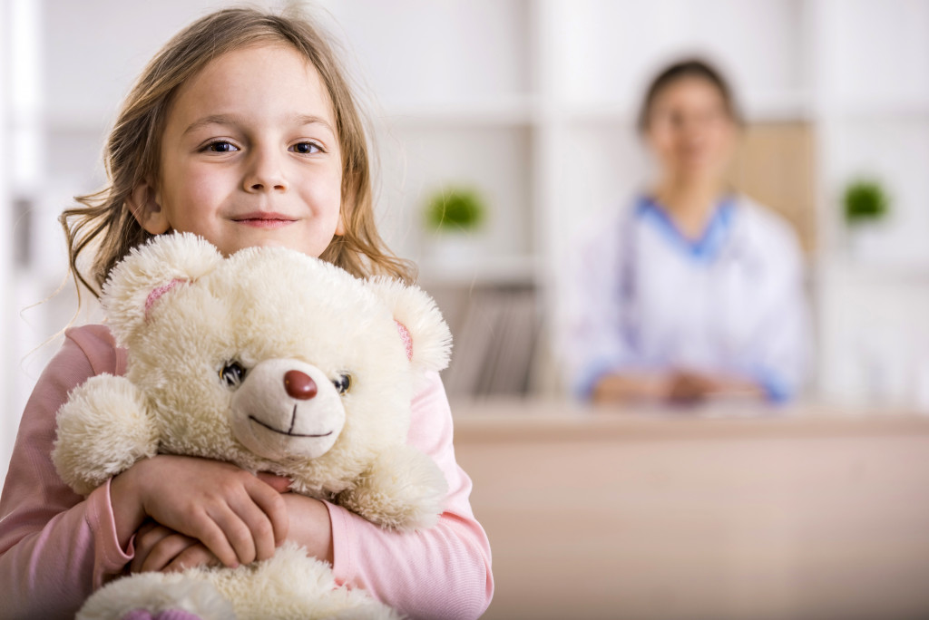kid holding a teddy bear with doctor on blur